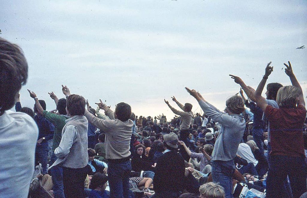 Photograph of a group of people cheering and making 'V' hand signs at the 'Isle of Wight Festival' (1969)
