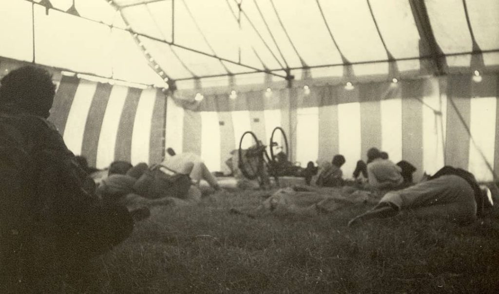 Photograph of multiple people resting on the grass inside a communal tent at the 'Isle of Wight Festival' (1969)