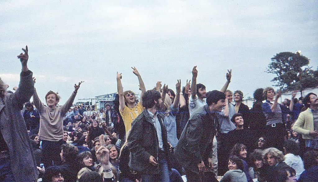 Photograph of a group of people cheering and making 'V' hand signs at the 'Isle of Wight Festival' (1969)