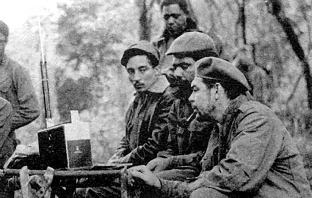 Listening to a Zenith Trans-Oceanic shortwave receiver are from left to right: Rogelio Oliva, José María Martínez Tamayo (known as 'Mbili' in the Congo and 'Ricardo' in Bolivia), and Ernesto 'Che' Guevara. Standing behind them is Roberto Sánchez ('Lawton' in Cuba and 'Changa' in the Congo) (1965)