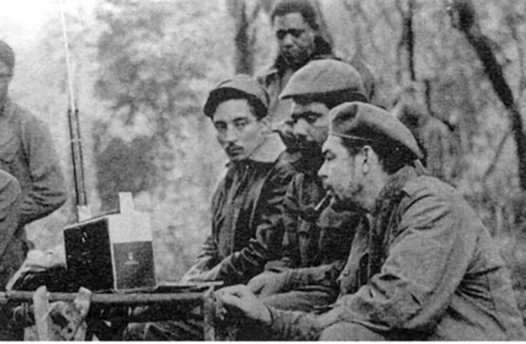 Listening to a Zenith Trans-Oceanic shortwave receiver are from left to right: Rogelio Oliva, José María Martínez Tamayo (known as 'Mbili' in the Congo and 'Ricardo' in Bolivia), and Ernesto 'Che' Guevara. Standing behind them is Roberto Sánchez ('Lawton' in Cuba and 'Changa' in the Congo) (1965)