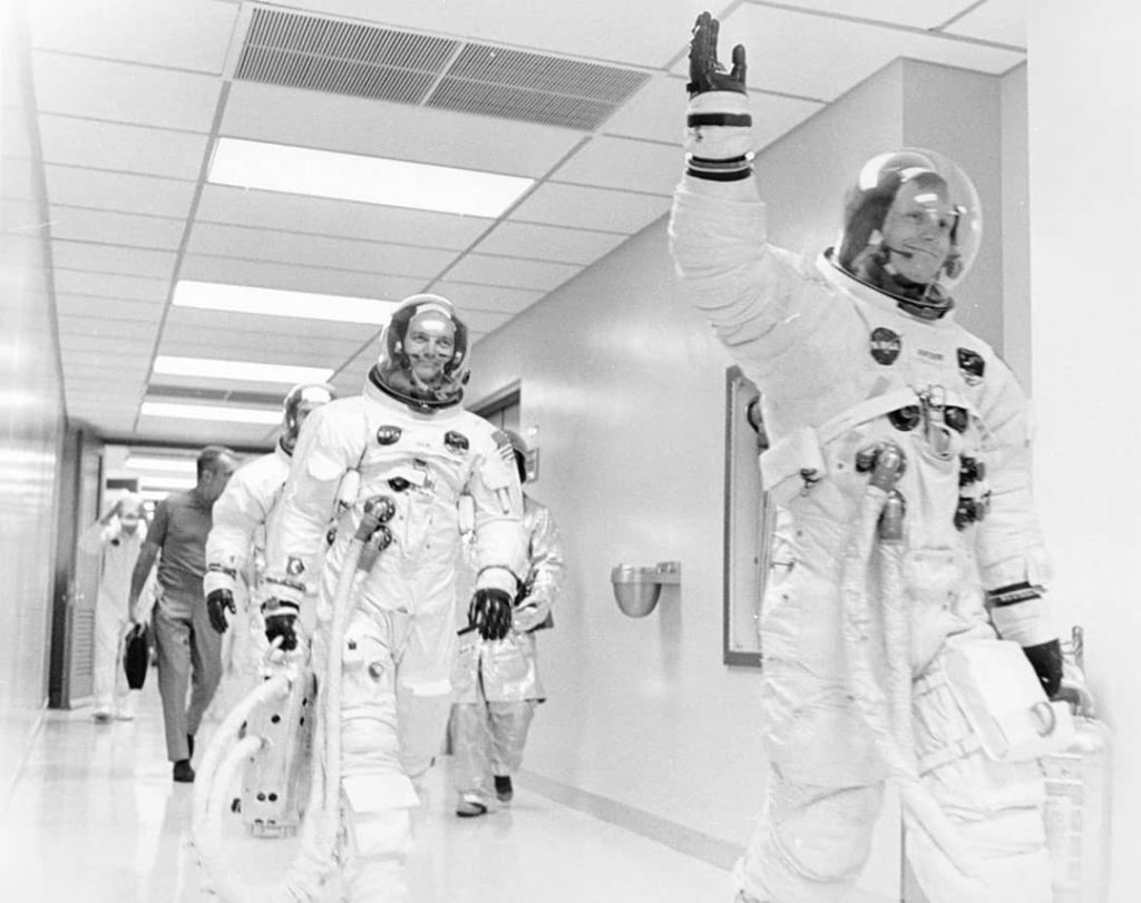 Neil A. Armstrong waving to well wishers on the way out to the transfer van. Mike Collins, Edwin E. 'Buzz' Aldrin Jr., and Deke Slayton follow right behind him (1969)