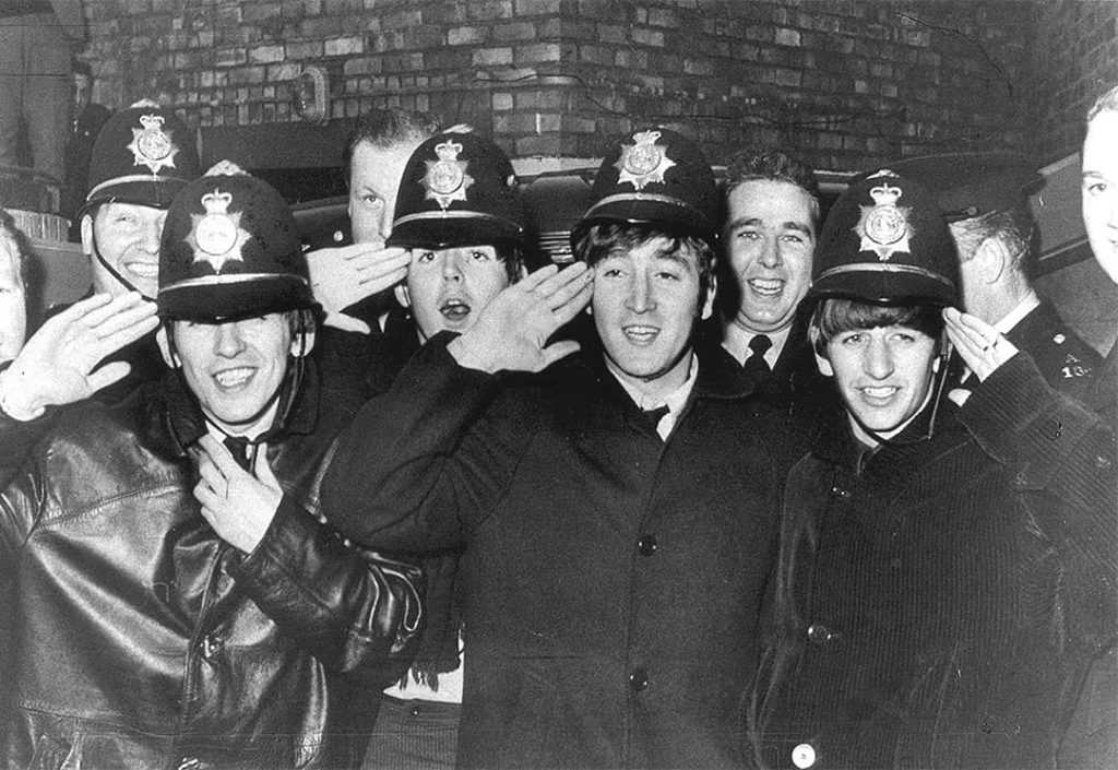 John Lennon with the rest of the Beatles posing with Birmingham police offices whilst wearing their 'bobbies' (1963)